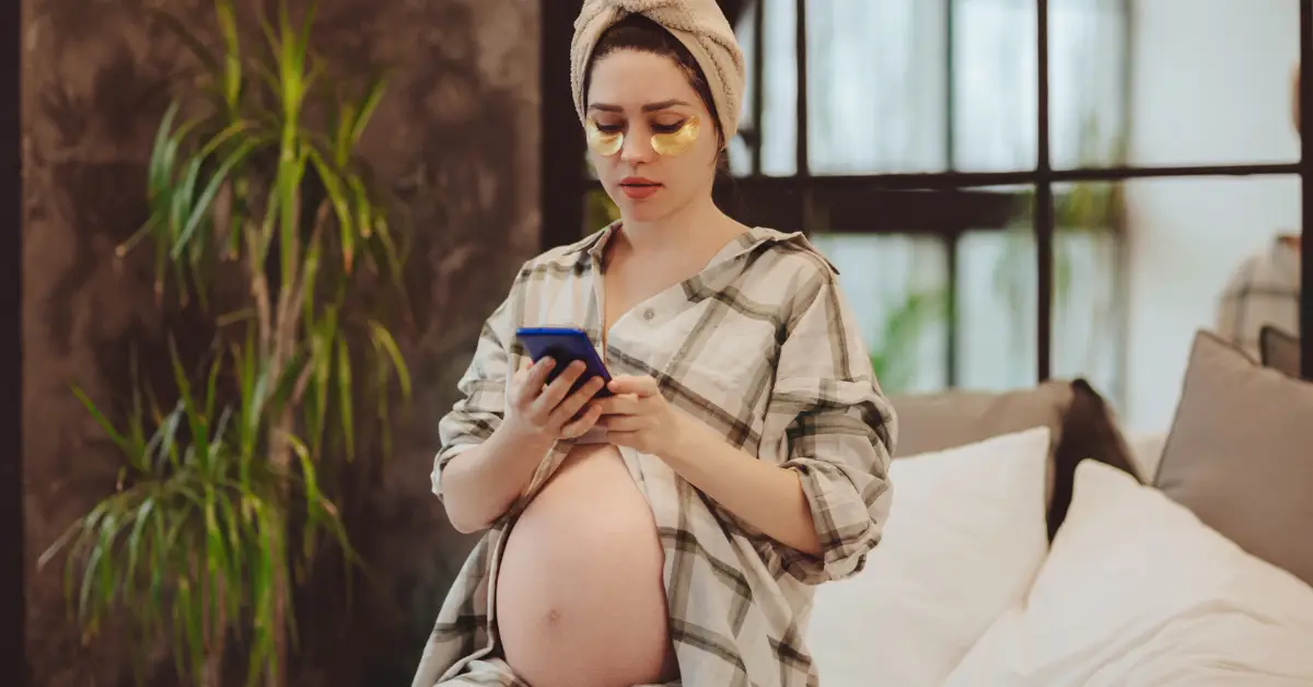 Pregnant women checking the little bean app on her phone if her eye patches are pregnancy safe